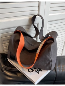 Large gray canvas crossbody bag with orange strap shown on a decorative book