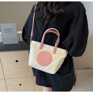 Detalle del bolso tote de nailon blanco roto con asas de cuero rosa y parche de logo