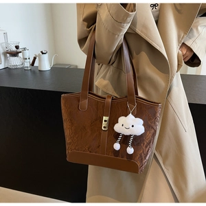 Detail of dark brown tote bag with leather textures and white cloud plush charm