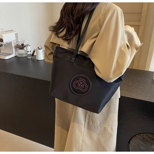 Detalle del bolso tote de nailon negro con logo rosa bordado en una cafetería