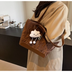 Detail of dark brown pleated tote bag with plush cloud charm in a cozy cafe setting