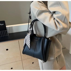 Detail of minimalist black leather bucket bag with geometric silk scarf and embossed logo