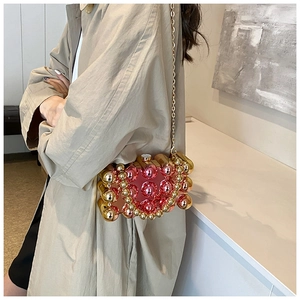 Detail of red acrylic clutch bag featuring golden metal beads and chain strap
