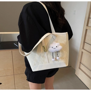 Detail of a creamy white tote bag with textured finish, gold clasp, and plush cloud charm