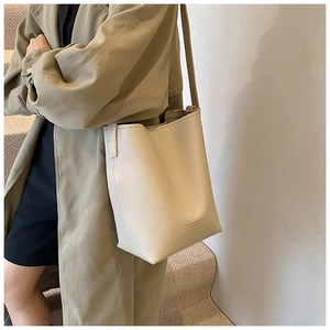 Detail of beige lychee pattern leather bucket bag with embossed logo on model