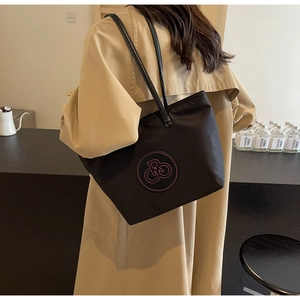 Detalle del bolso tote de nailon negro con logo bordado rosa llevado por modelo en gabardina
