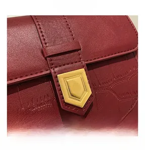 Detail of burgundy crocodile embossed leather saddle bag with gold metal buckle