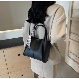 Detail of a black leather bucket bag featuring a silk scarf and detachable shoulder strap