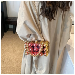 Detail view of acrylic evening bag with pink and gold spheres on model's shoulder