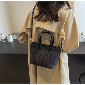 Primer plano del bolso tote de nailon negro con logo bordado rojo y detalles metálicos dorados