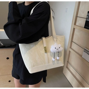 Detail of off-white tote bag with wrinkled texture, metal lock, and plush cloud charm