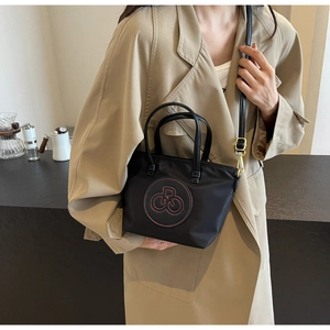 Detalle del bolso tote de nailon negro repelente al agua con costuras rojas y correa de cuero