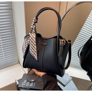 Close-up of black leather bucket bag with silk scarf detail and brand logo engraving