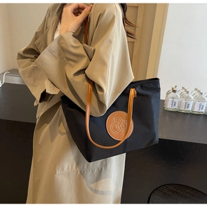 Detalle del bolso tote de gran capacidad con cuerpo de nailon negro y parche de cuero marrón
