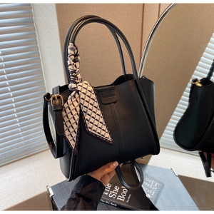 Detail of black bucket bag featuring a geometric silk scarf handle and logo tag detail