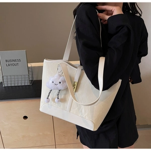 Detail of cream patent leather tote bag with plush cloud charm and gold metal buckle