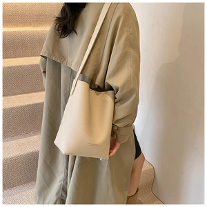 Detail view of beige pebbled leather bucket bag with fashion text on trench coat model