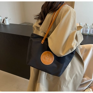 Bolso tote de nailon negro con correas de cuero marrón y logo llevado por una modelo