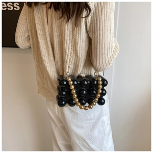 Macro shot of black acrylic beaded box bag with gold chain and round pearl handle