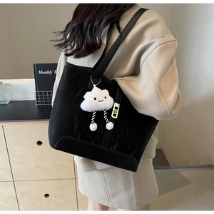 Detail of black pleated tote bag with golden lock and cute white plush charm accessory