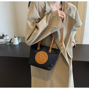 Detalle de un mini bolso tote de nailon negro con asas de cuero marrón en una modelo