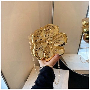 Detail of a golden flower-shaped evening clutch bag with high-gloss metallic finish and chain