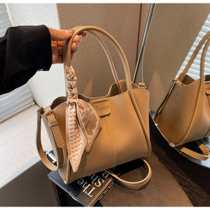 Detail of khaki bucket bag with silk scarf on handle and embossed logo on the front