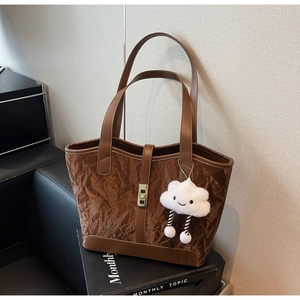 Detail of a brown pleated tote bag with smooth leather trim and a white cloud plush charm