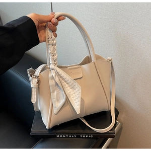 Detail showing elegant off-white bucket bag with decorative silk scarf and logo