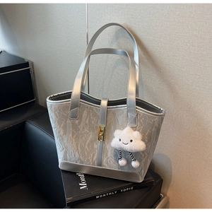 Detail of silver tote bag featuring pleated texture, gold buckle and plush cloud charm