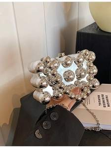 Silver metallic spherical evening bag with chain strap held by a model in a suit