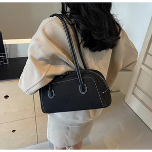 Close-up of black matte shoulder bag featuring white contrast stitching and slim straps