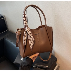 Brown leather tote bag detail with decorative silk scarf and metallic handle hardware
