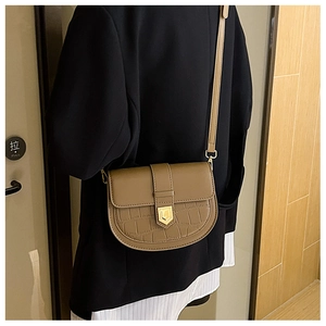 Model wearing a khaki saddle bag with crocodile texture and golden shield buckle