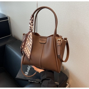 Detail of brown leather bucket bag with silk scarf and logo on modern background