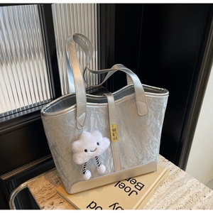 Detail of silver textured tote bag featuring a gold square buckle and cloud plush charm