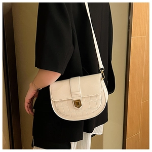 Close-up of beige saddle bag with crocodile texture and golden shield buckle detail