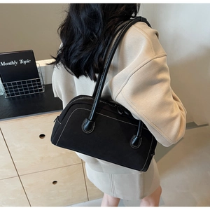 Detail of black suede bag featuring contrast white stitching and minimalist baguette design