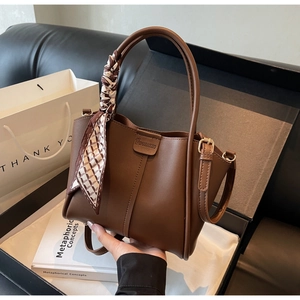 Detail of dark brown leather bucket bag with top handles and patterned silk scarf