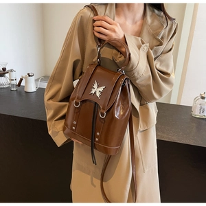 Detail of a brown glossy leather backpack with a decorative silver butterfly buckle