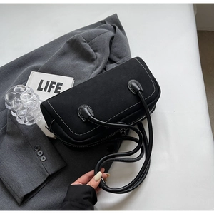 Detail of black suede Boston bag with white contrast stitching on grey blazer background