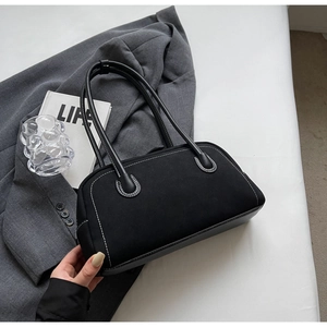 Detail of black suede handbag featuring contrasting white stitching and slender handles