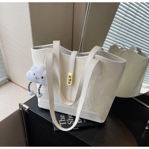 Detail of a creamy white textured tote bag with golden lock and plush cloud charm