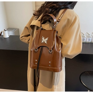 Close-up of caramel leather backpack with silver butterfly detail on the back of a model