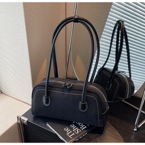 Close-up of black baguette bag with white contrast stitching and round top handle