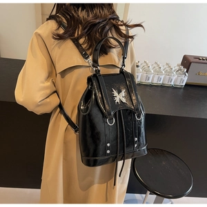 Detail of glossy black leather backpack with silver butterfly ornament and drawstring closure