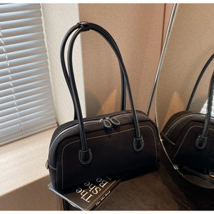 Close-up of retro black shoulder bag with contrast white stitching and long handles