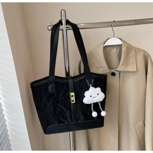 Detail of black pleated tote bag with golden lock and white plush cloud charm on a strap
