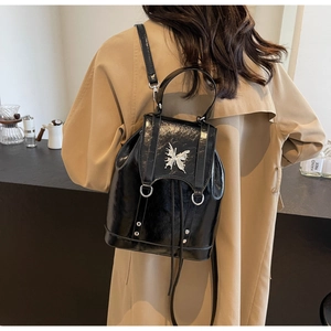 Detail of black glossy backpack with silver butterfly hardware on model in a cafe