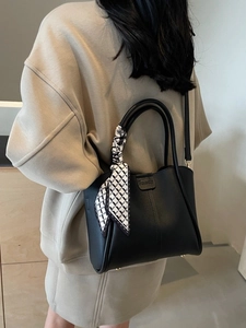 Elegant black faux leather bucket bag with decorative scarf and logo, worn by a model